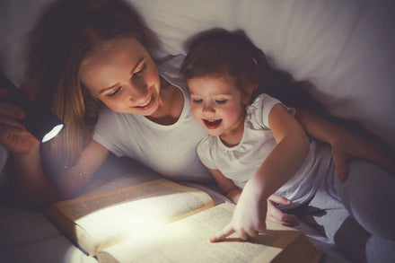 Mother and daughter reading a book with a lantern at nighttime.