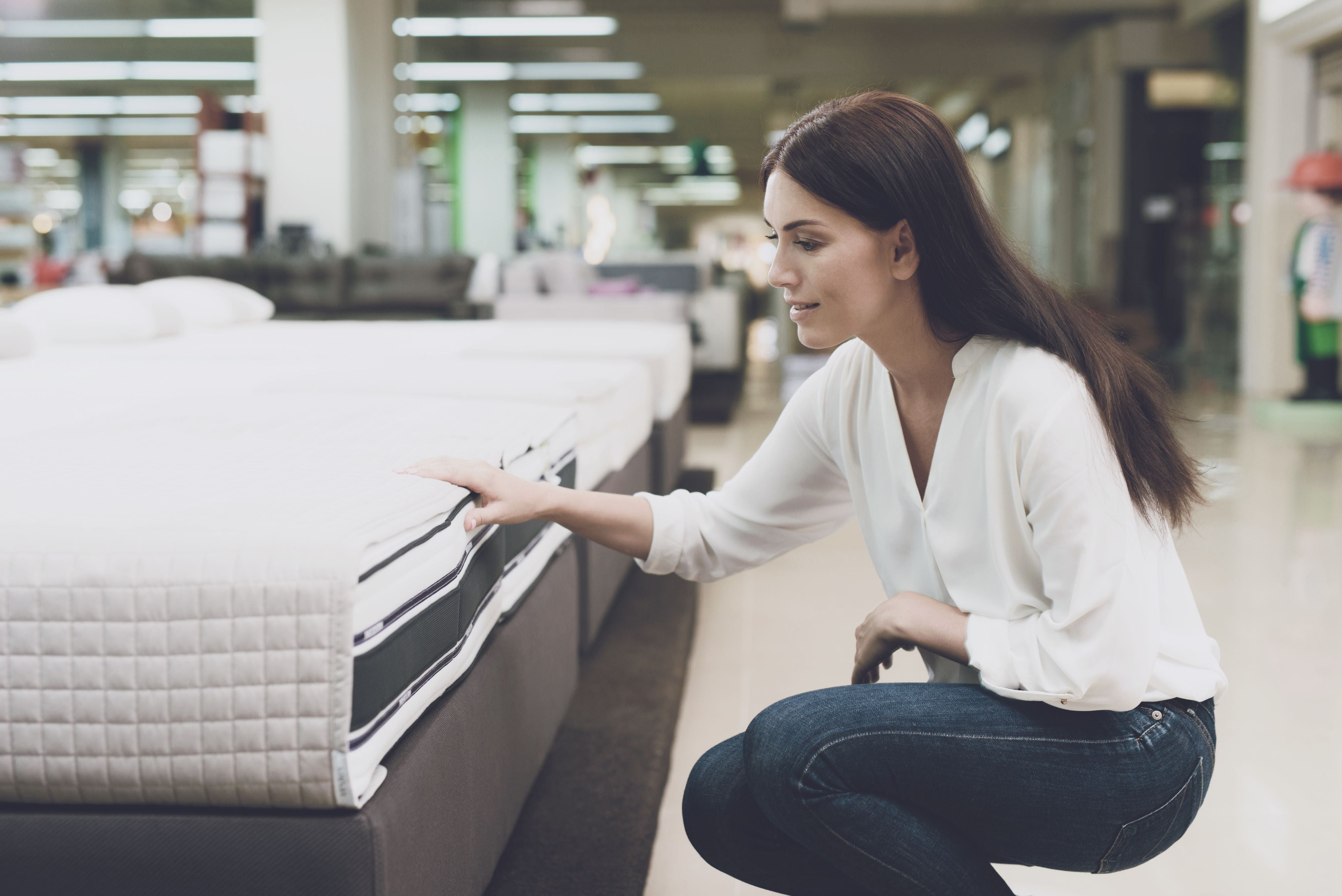 A woman chooses a mattress in a store, she sits next to it and examines it