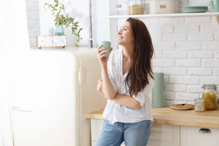 A woman leaning against a kitchen counter enjoying a drink in a mug.
