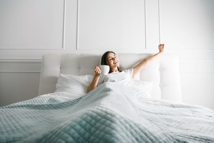 Woman waking up in bed with a cup of coffee