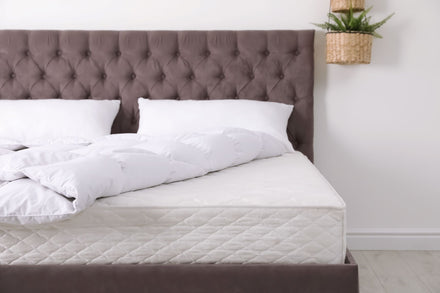 A bed with a gray headboard and a clean mattress without sheets.