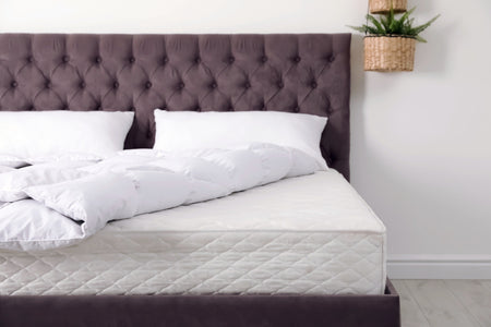A bed with a gray headboard, white bedding and a white wall behind.