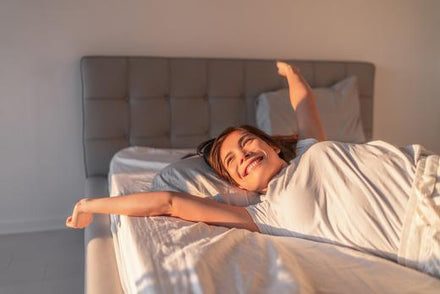A woman smiling and stretching in her bed.