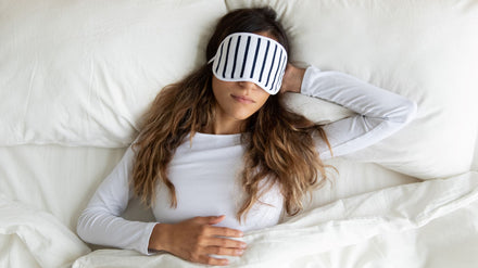 Woman sleeping with a sleep mask and one hand behind her head.