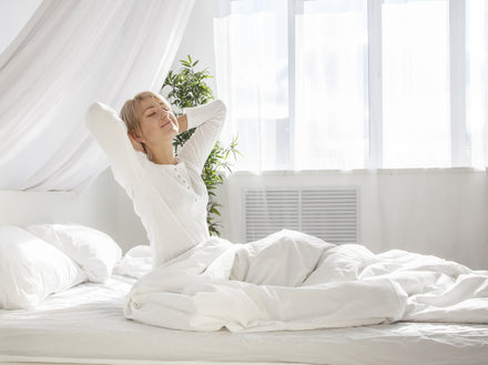 A woman sitting in her bed waking up in a sunny day.