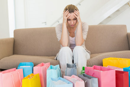 A worried woman with her hands on her head in front of shopping bags.