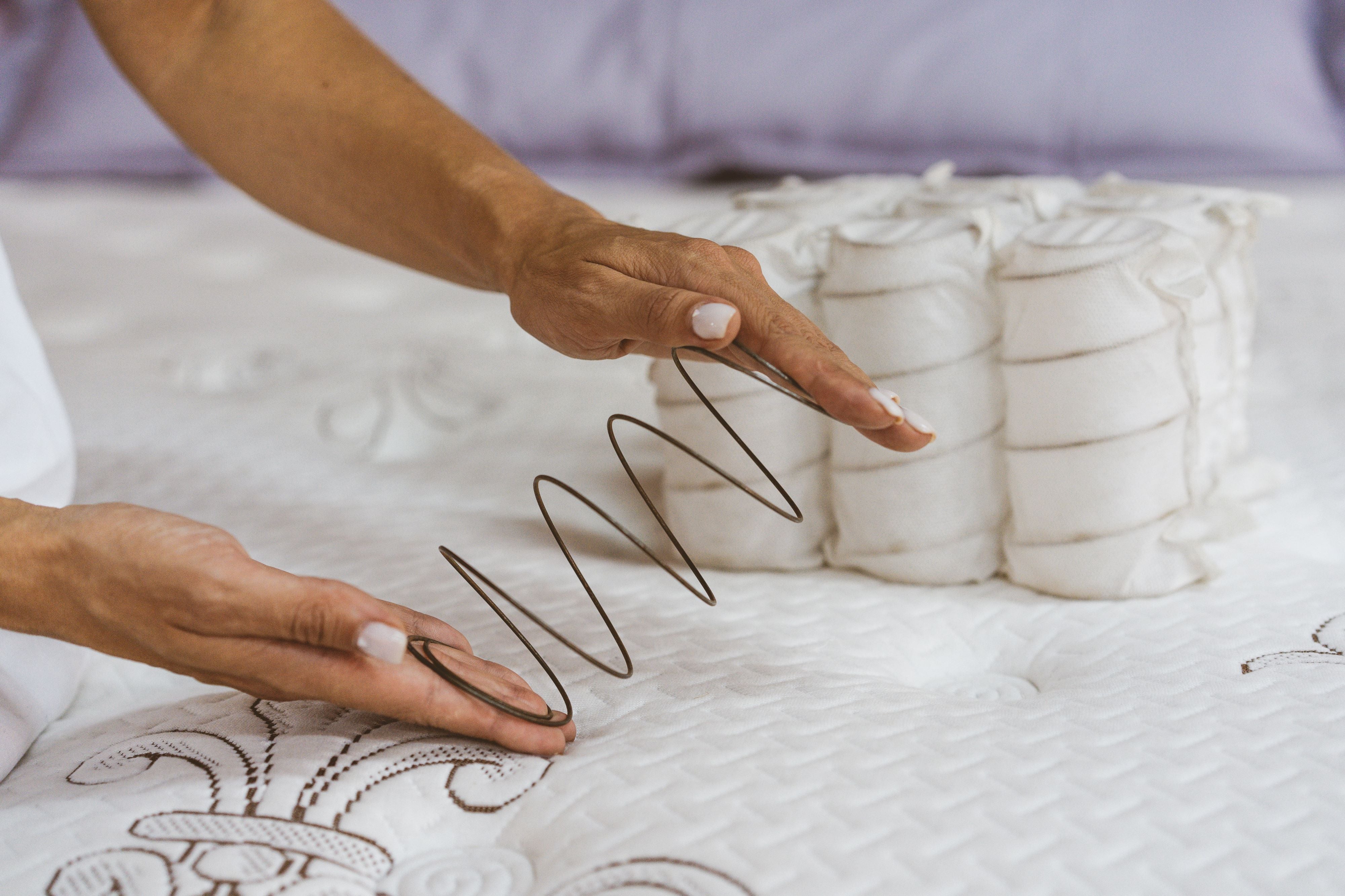A woman holds a mattress spring in her hands. Pocketed coils are shown in the background of the photo.