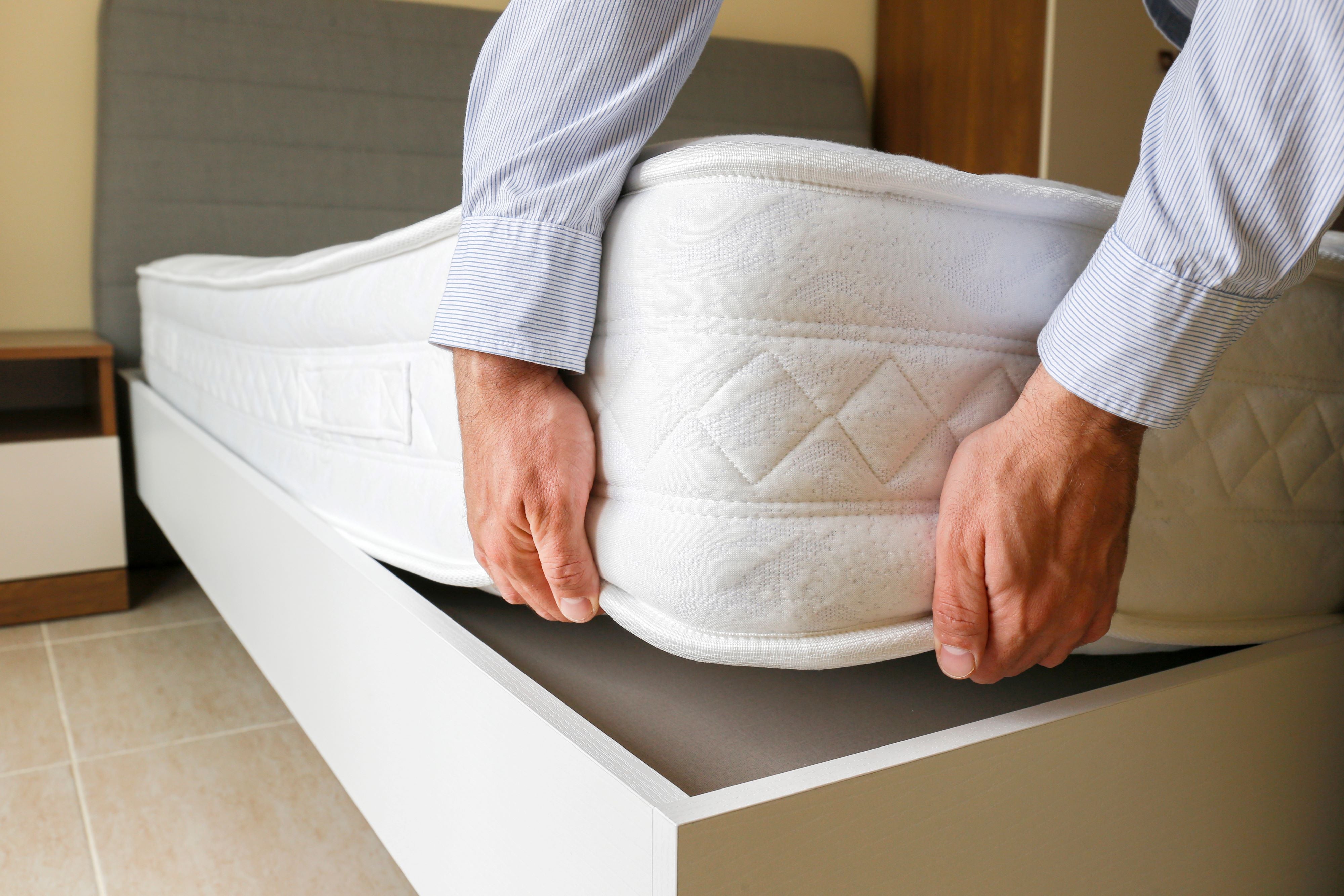 Close up of a man lifting the corner of an innerspring mattress off the base.