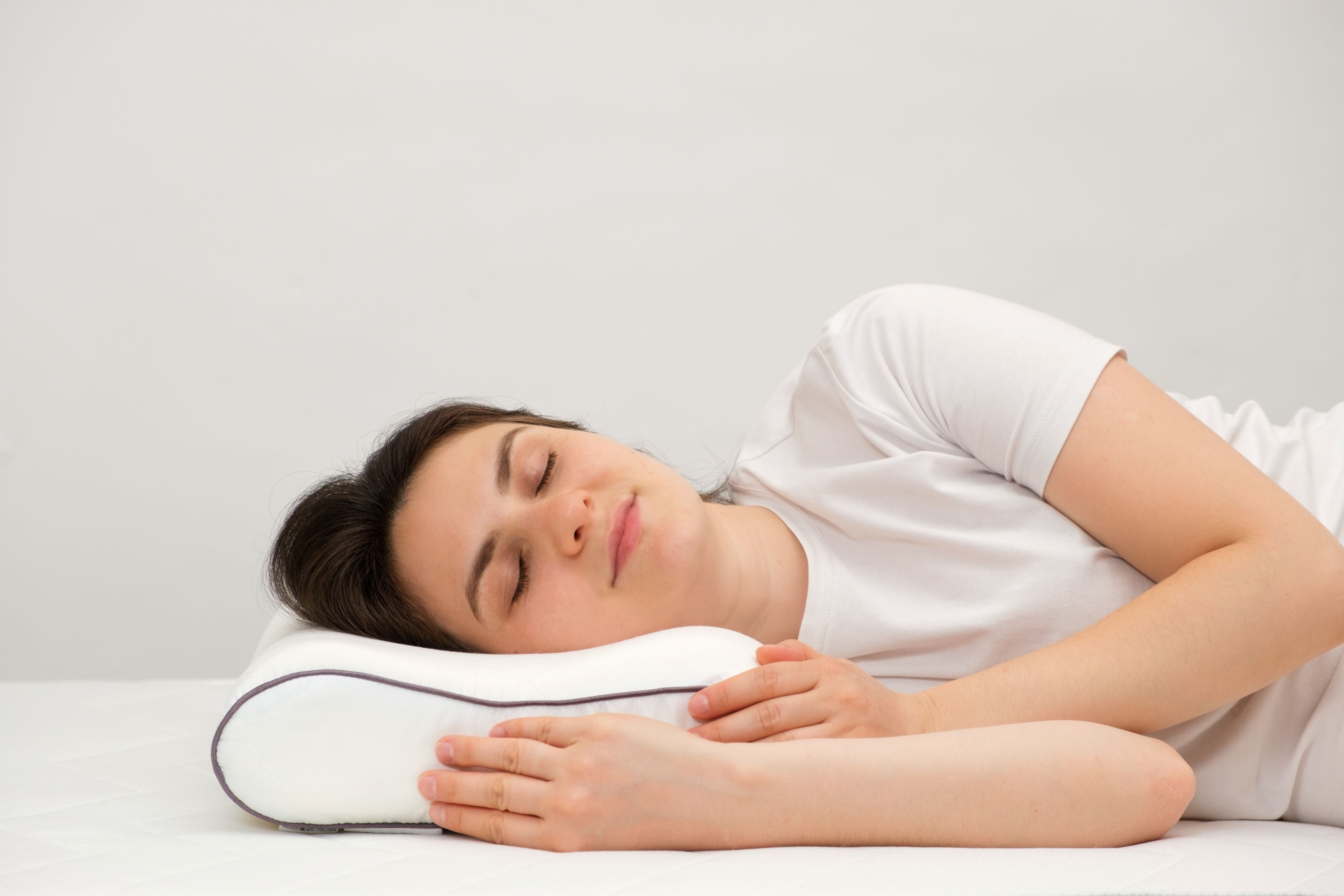 A woman sleeps comfortably on an orthopedic pillow made of memory foam, lying on a bed.